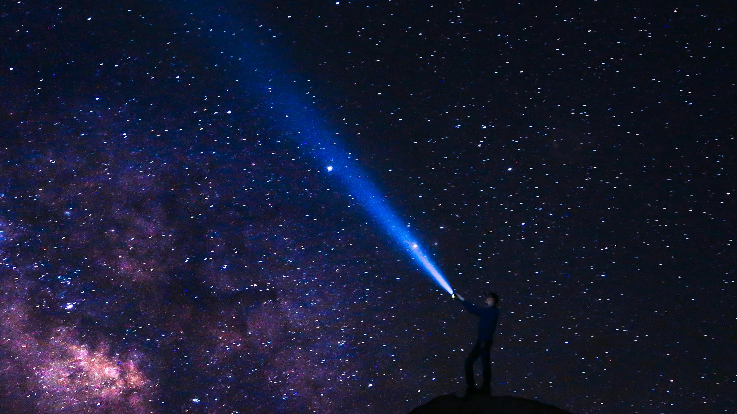 A person shines a flashlight against a dramatic starry night sky