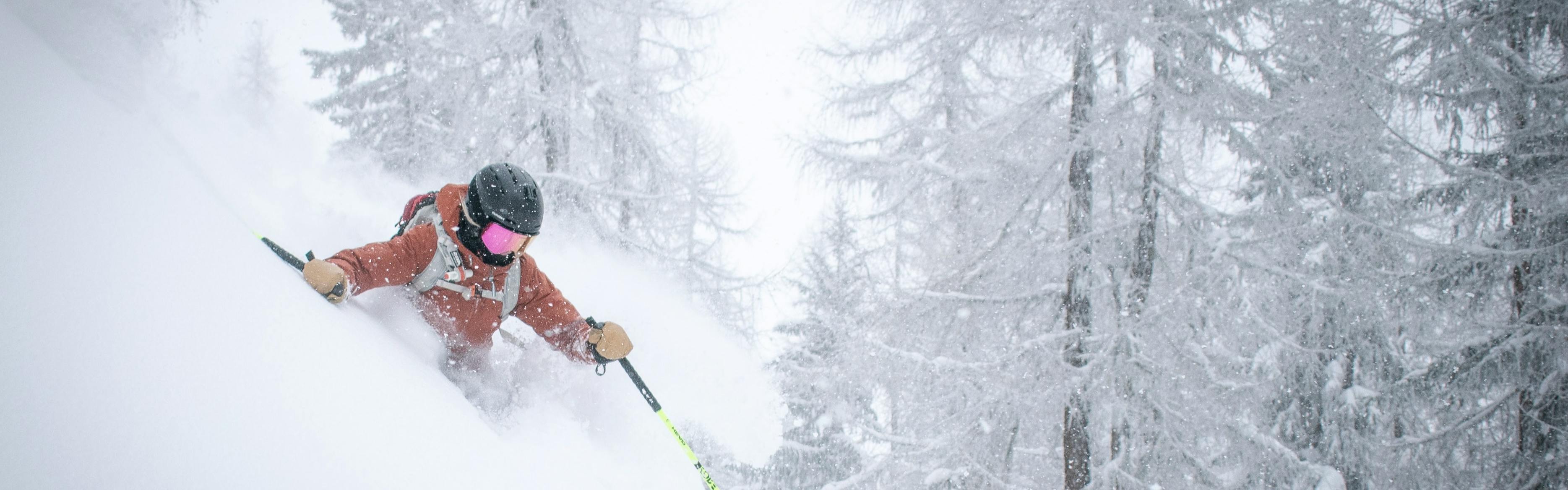 A skier in an orange jacket skis some deep powder.