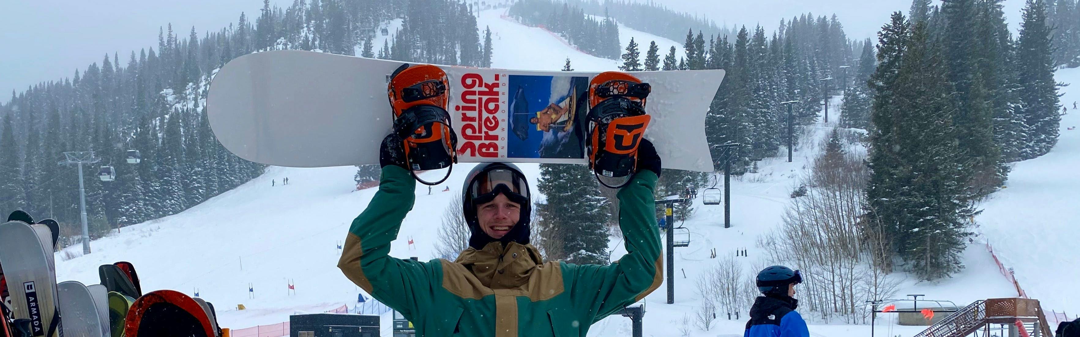 A snowboarder holding up the CAPiTA Spring Break Slush Slasher Snowboard · 2023.