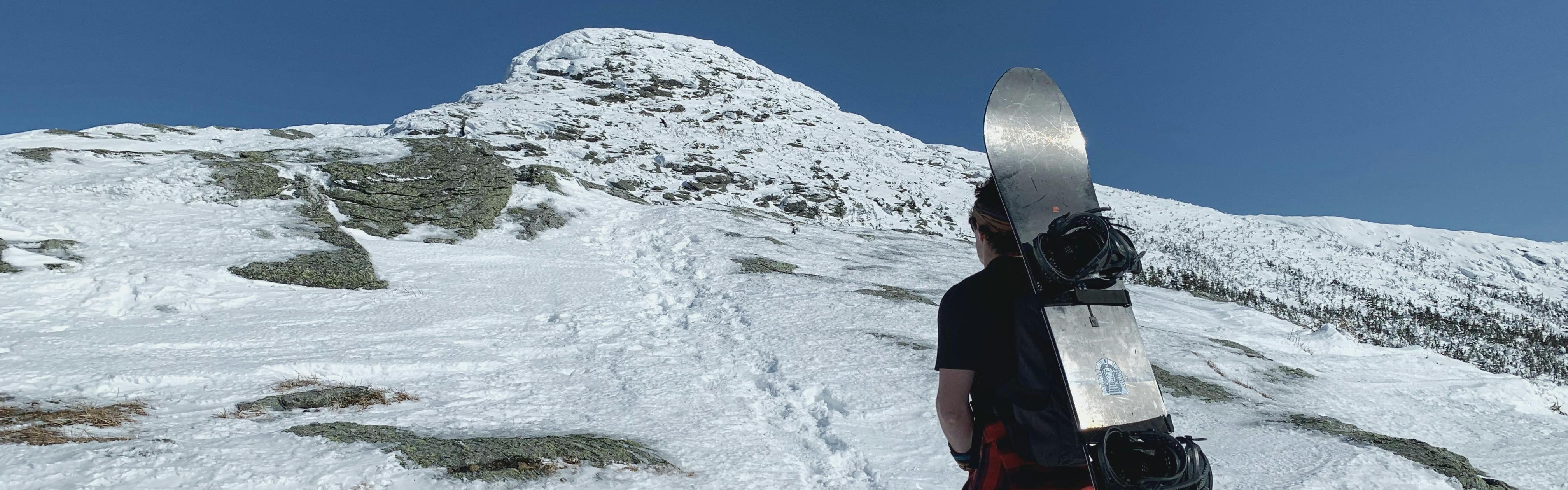 A man hikes up a mountain with a snowboard on his back