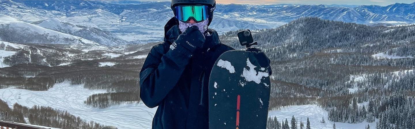 A snowboarder standing with his snowboard and wearing the Burton AK GORE-TEX Clutch Mitt.