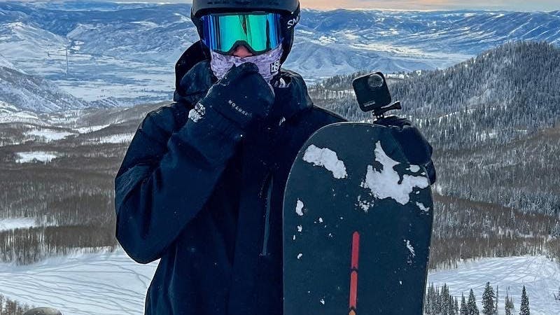 A snowboarder standing with his snowboard and wearing the Burton AK GORE-TEX Clutch Mitt.