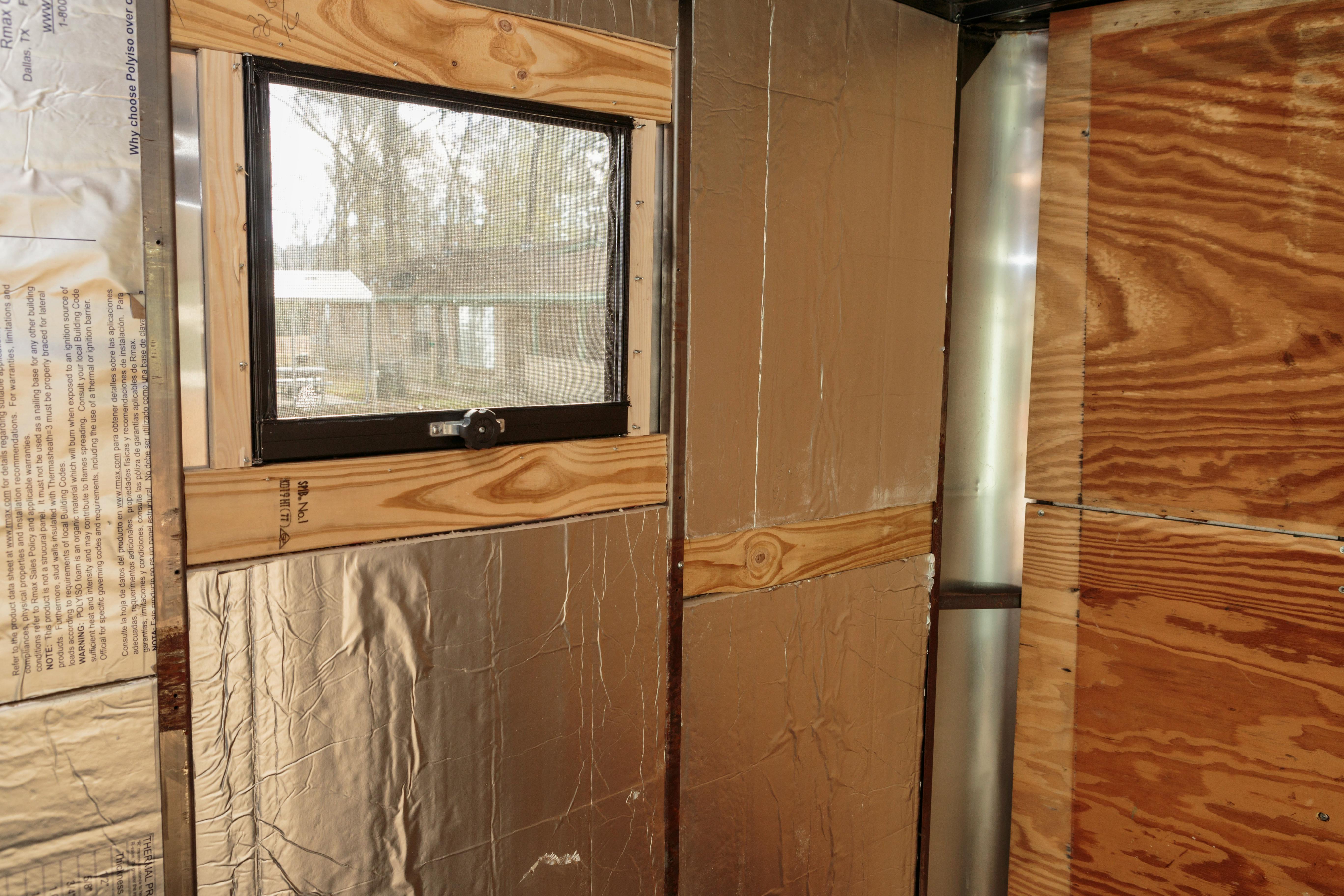 A window in a cargo trailer. It is surrounded by wood and insulation.
