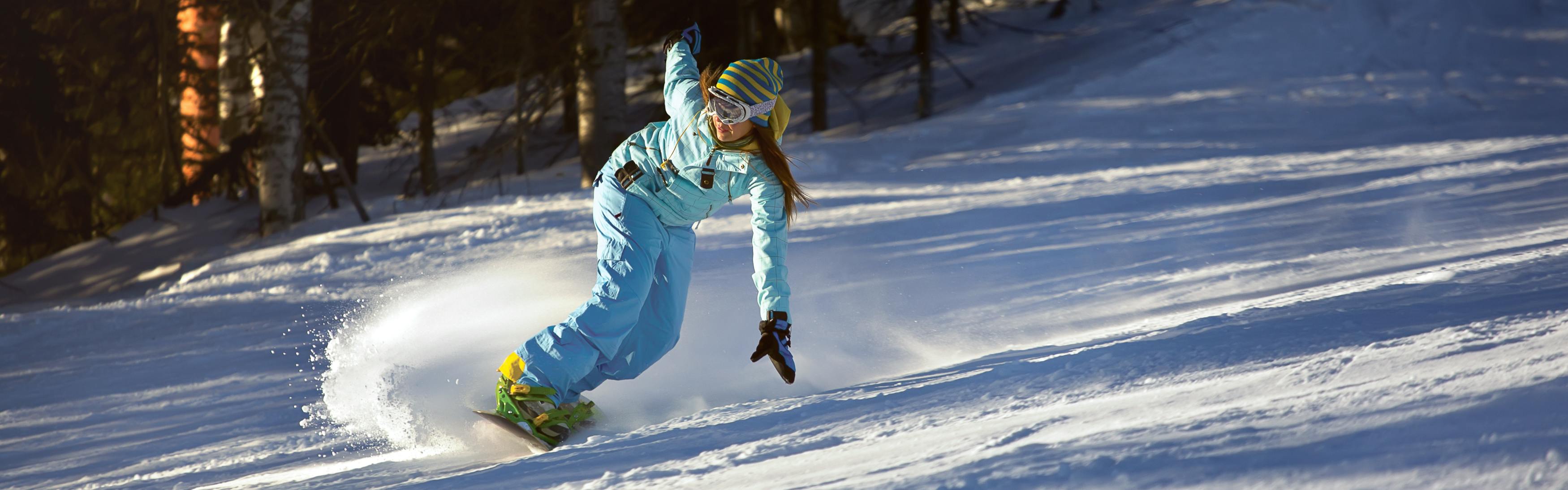 A female snowboarder carves down an icy slope on her snowboard. 
