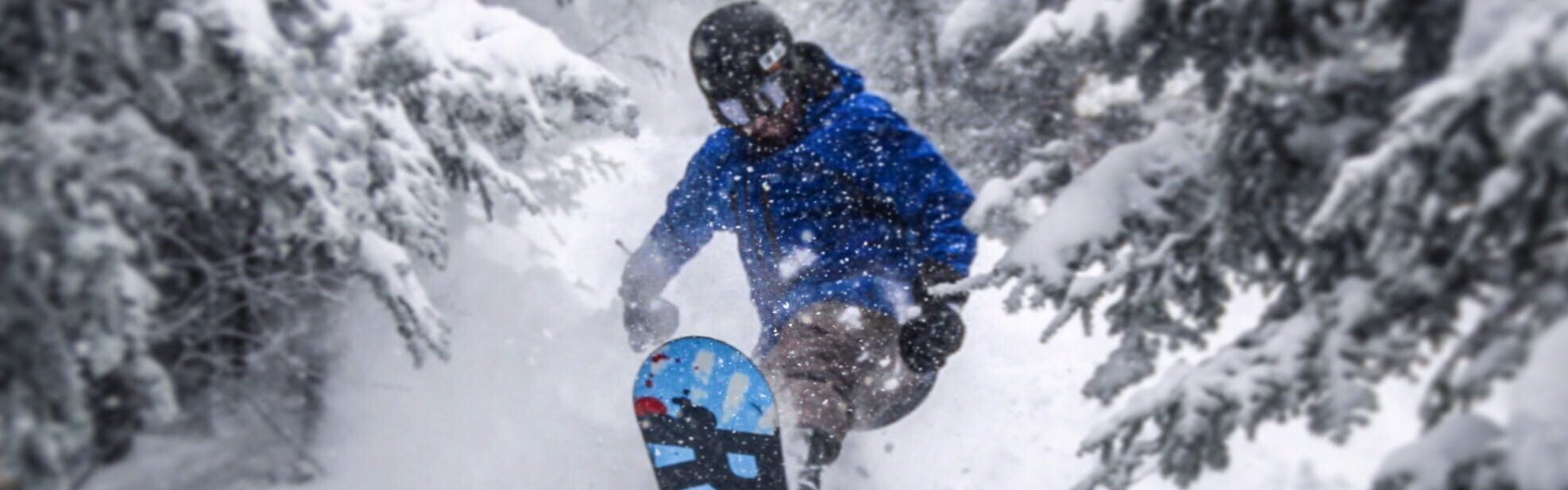 Curated expert Luke Sussdorf launching a jump in powder in the forest