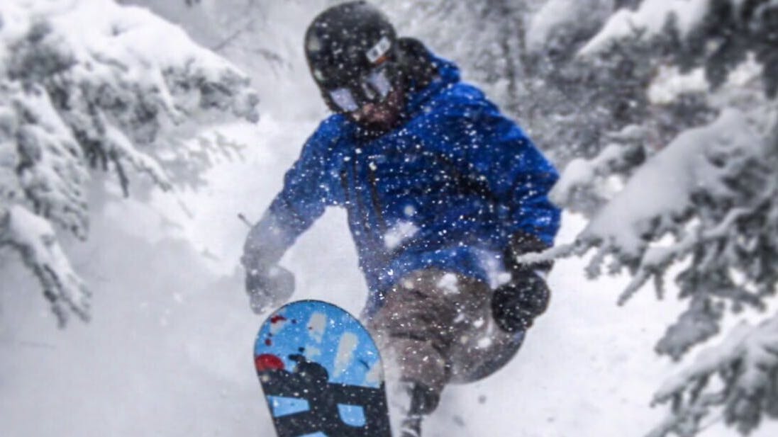 Curated expert Luke Sussdorf launching a jump in powder in the forest