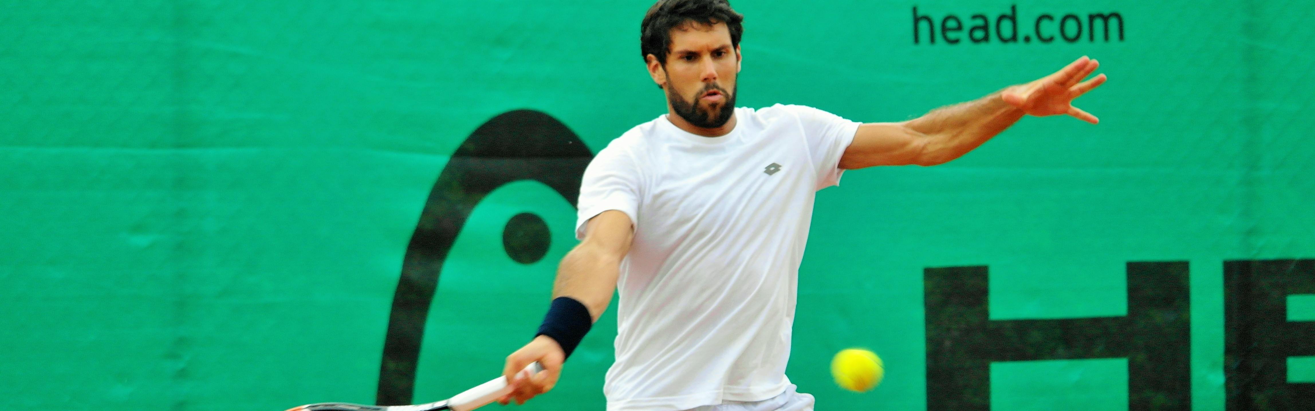 A tennis player wearing a lotto brand shirt hitting a tennis ball.