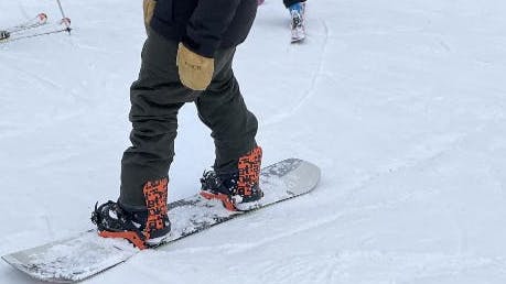 A snowboarder standing on his snowboard while wearing the Volcom Men's Roan Bib Pants.