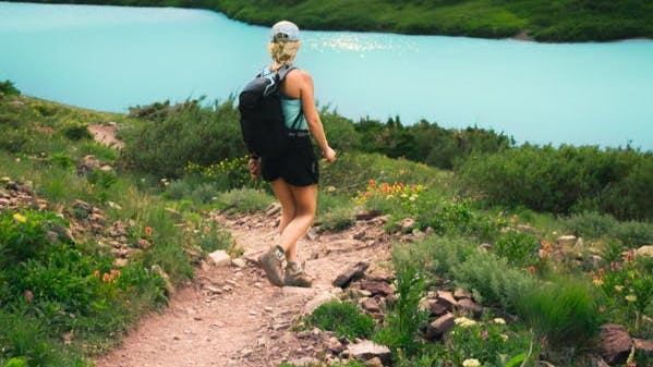 A hiker walking along a trail to a blue lake. 