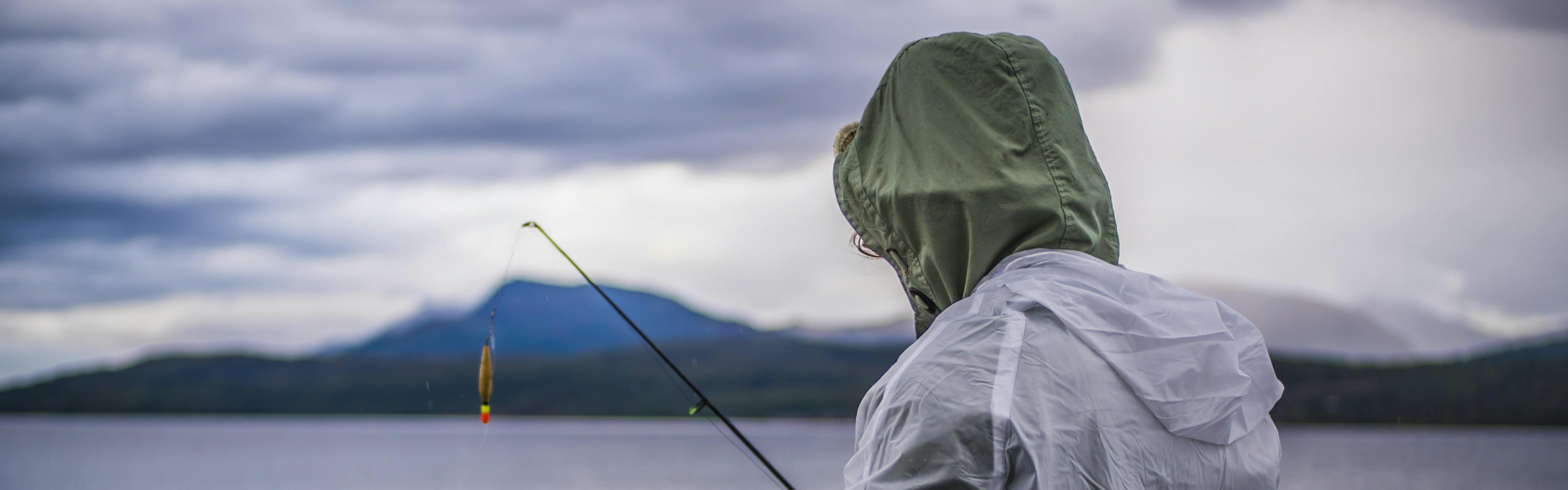 Someone fishes while wearing two raincoats. 
