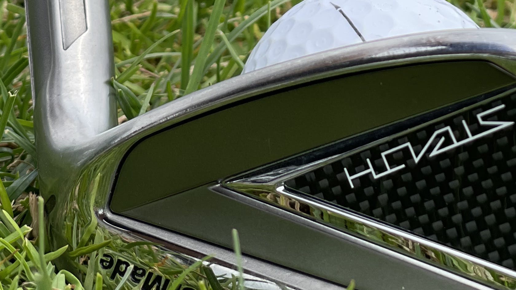 The TaylorMade Stealth Iron in front of a ball in some grass.
