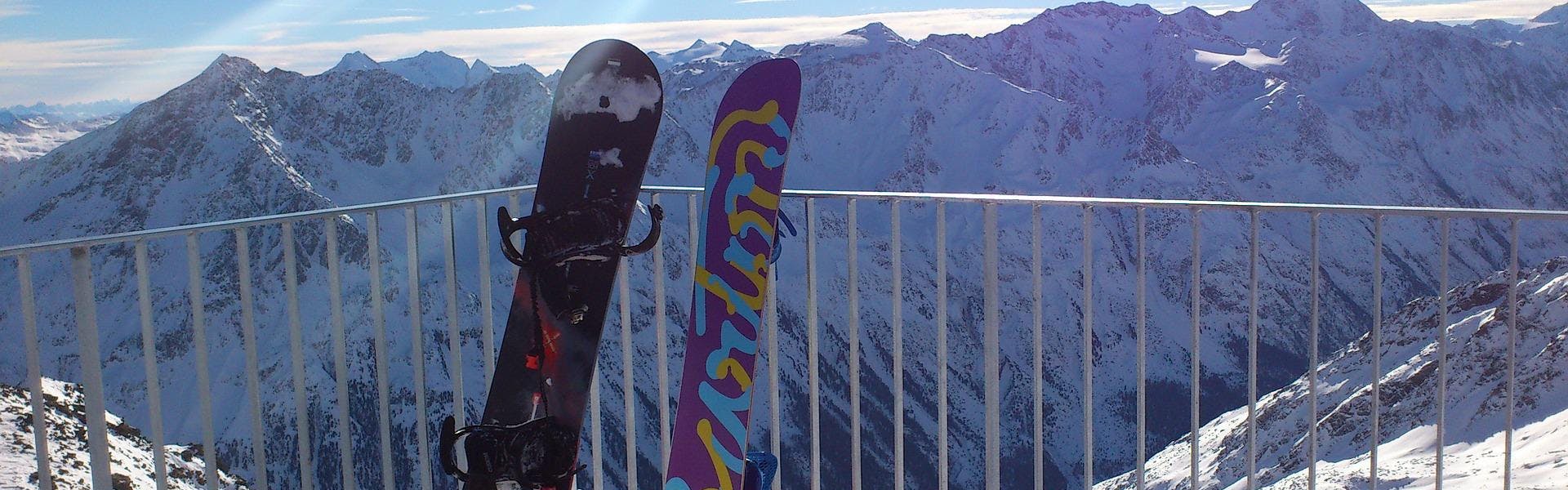 Two snowboards rest against a railing with mountains in the background.