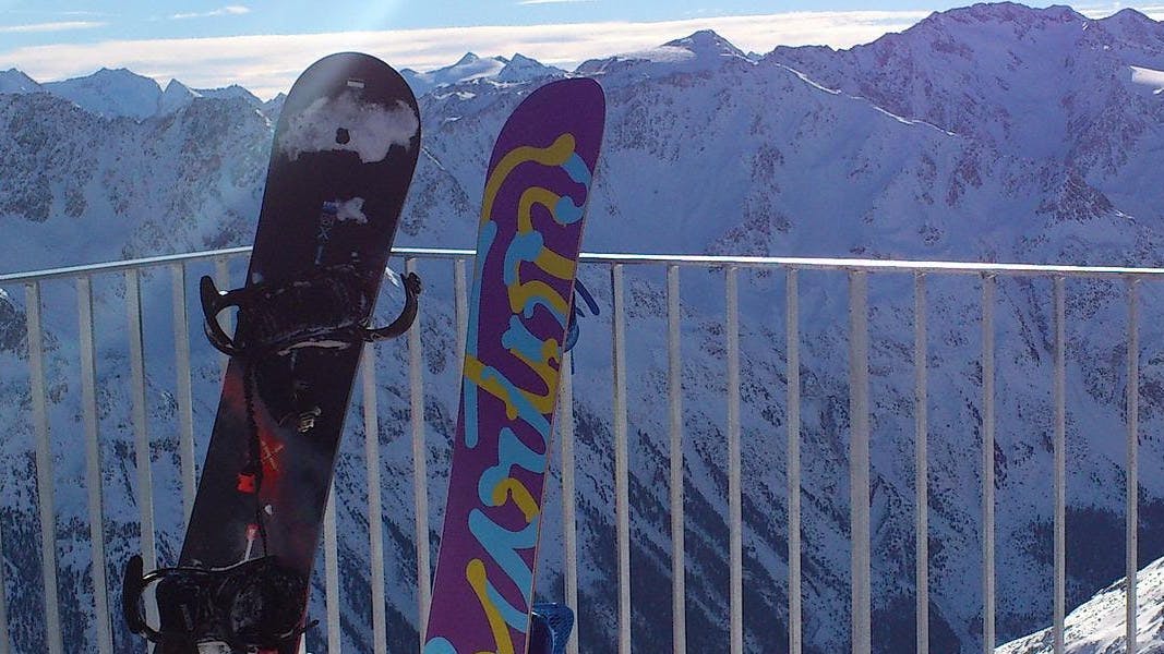 Two snowboards rest against a railing with mountains in the background.