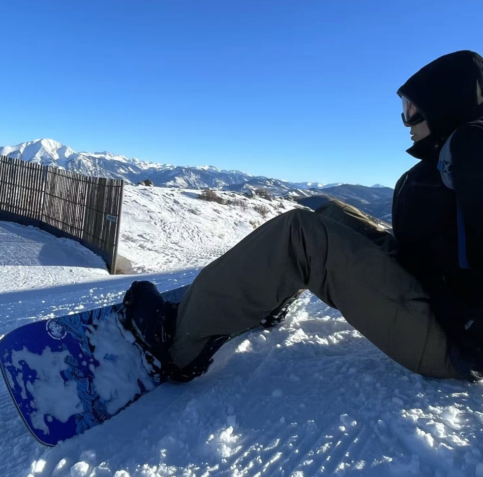 A snowboarder sits on the ground with his snowboard attached to his feet.
