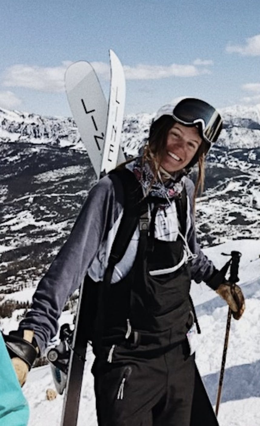 A woman standing with the Line Pandora 104 skis on her backpack. 