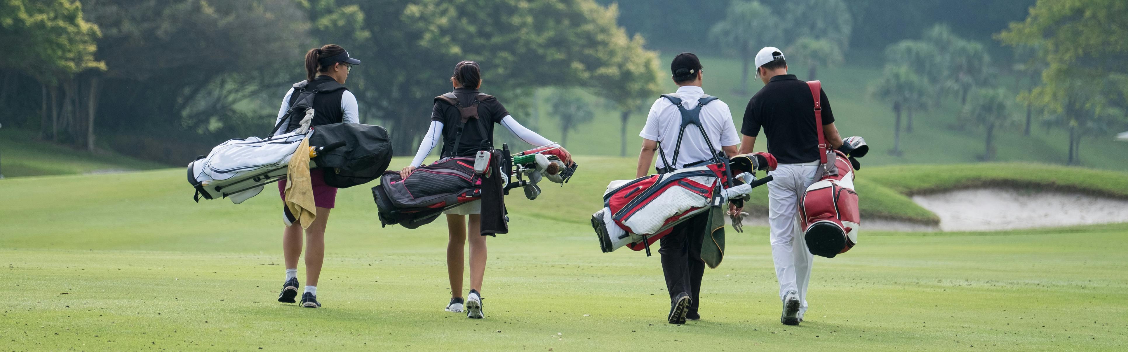 Four people carrying golf bags walk away from the camera towards the green