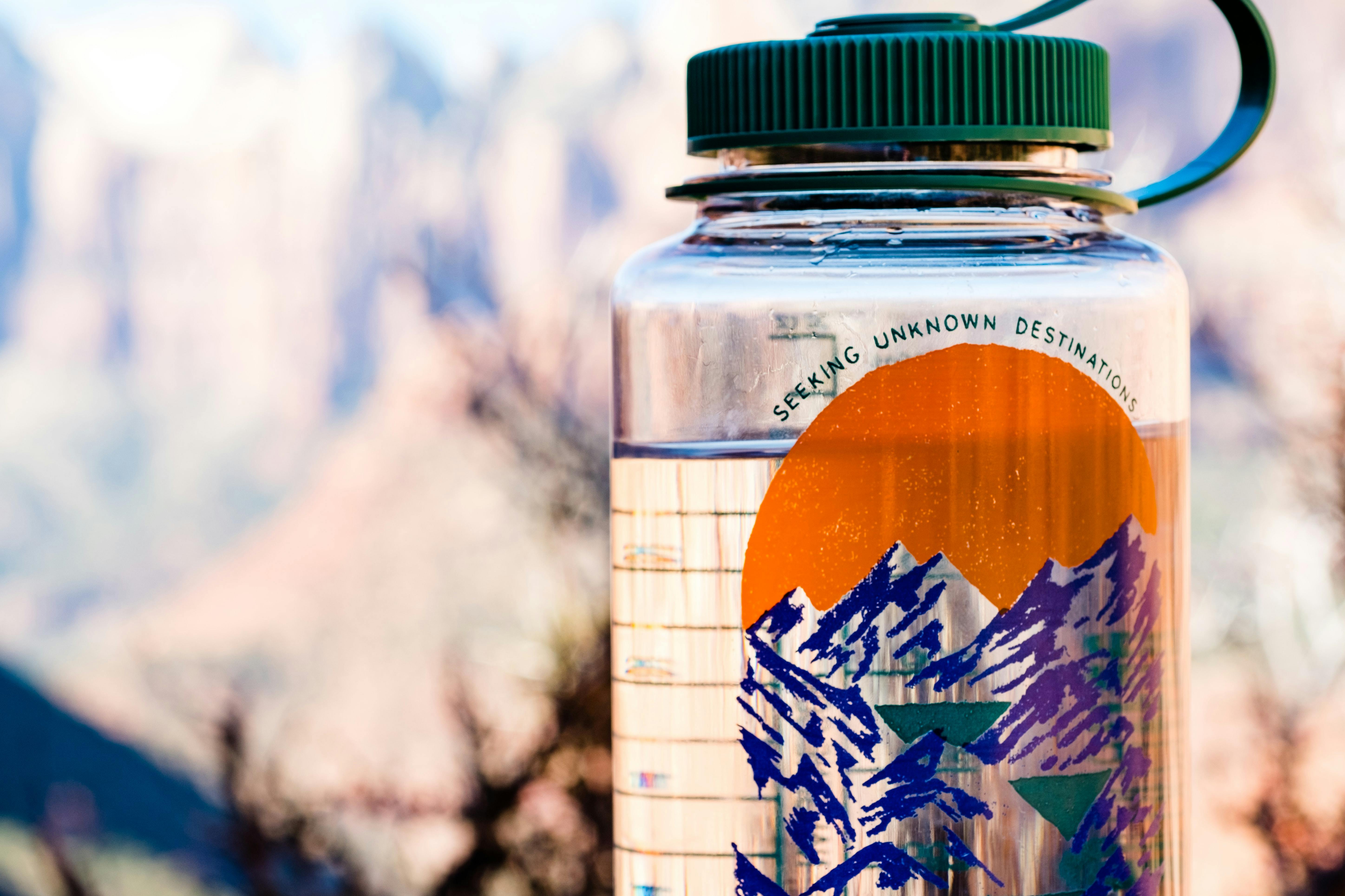 A clear Nalgene water bottle with a green lid and a mountain graphic that says "Seeking Unknown Destinations" on it.
