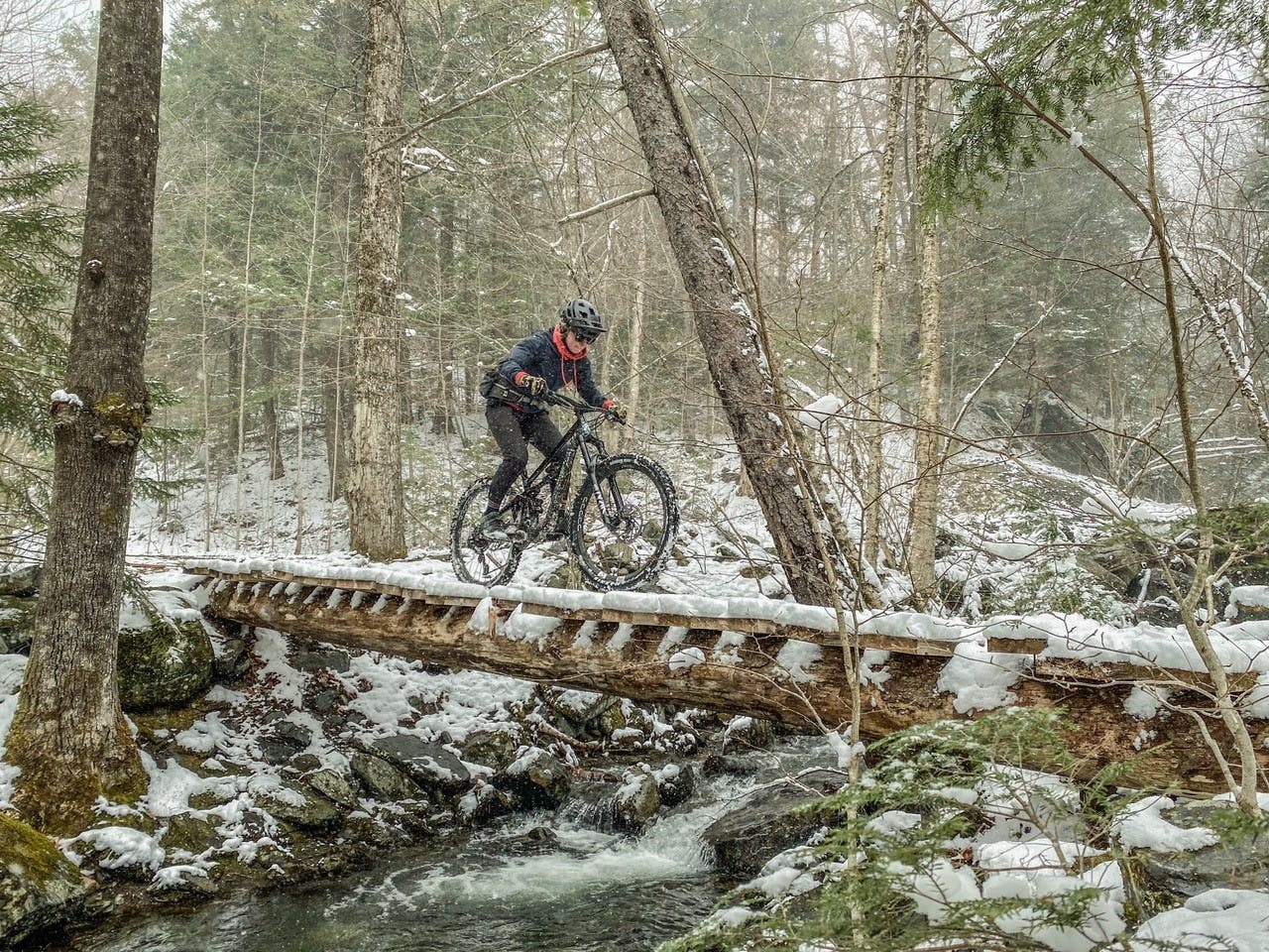 Woman crossing a wooden bridge over a creek in a blizzard on her mountain bike.