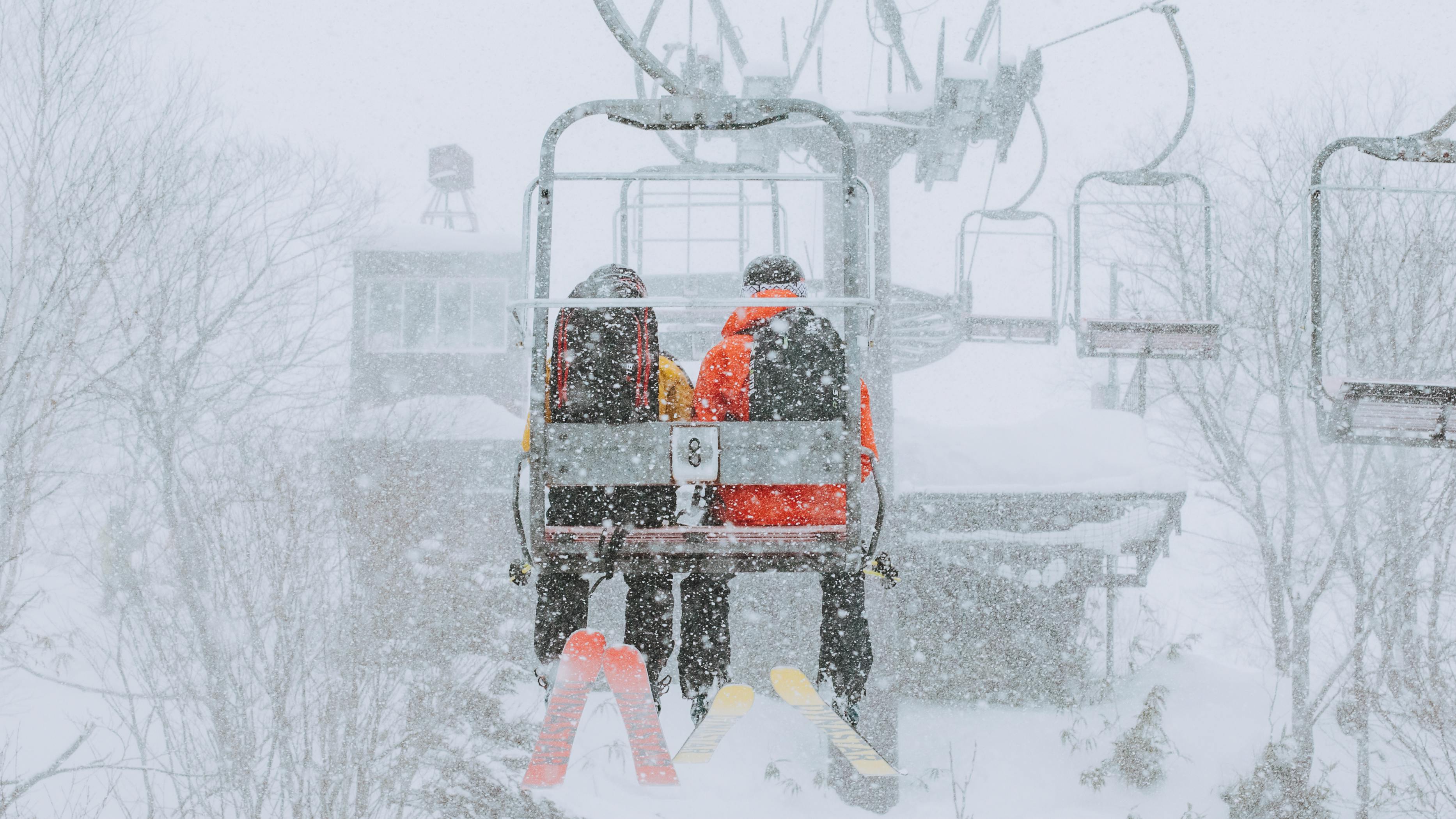 Two skiers sit on a chairlift on a snowy day.