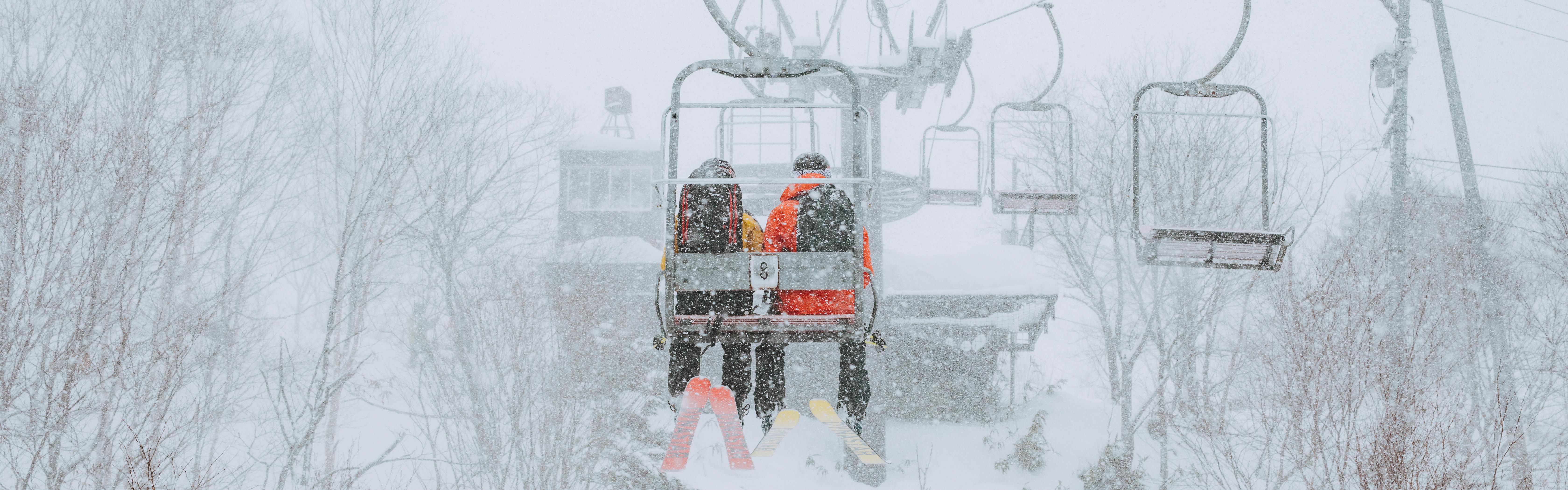 Two skiers sit on a chairlift on a snowy day.