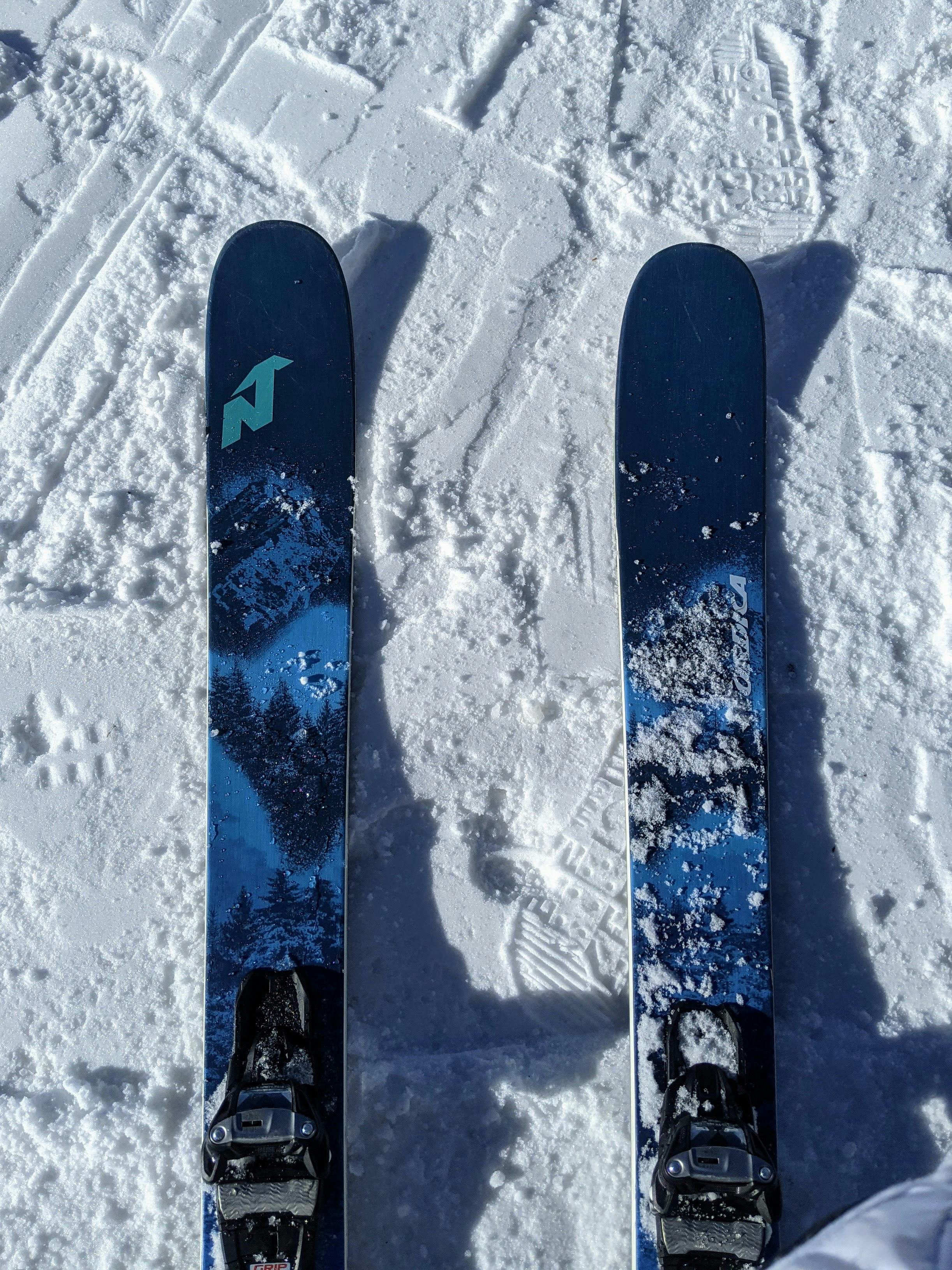 Top down view of some Nordica skis with bindings. They are laying on top of snow. 