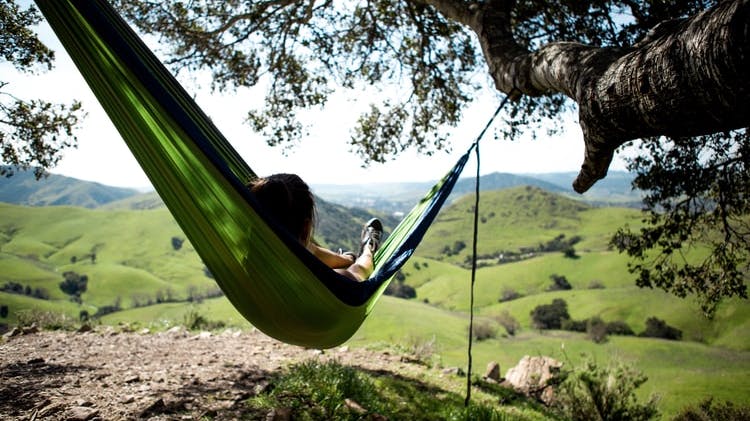 A person lies in a hammock while looking out at rolling green hills