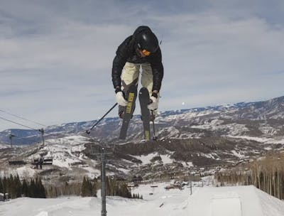 Curated Expert Jake Renner doing a Truck Driver 3 trick off a jump on skis. 