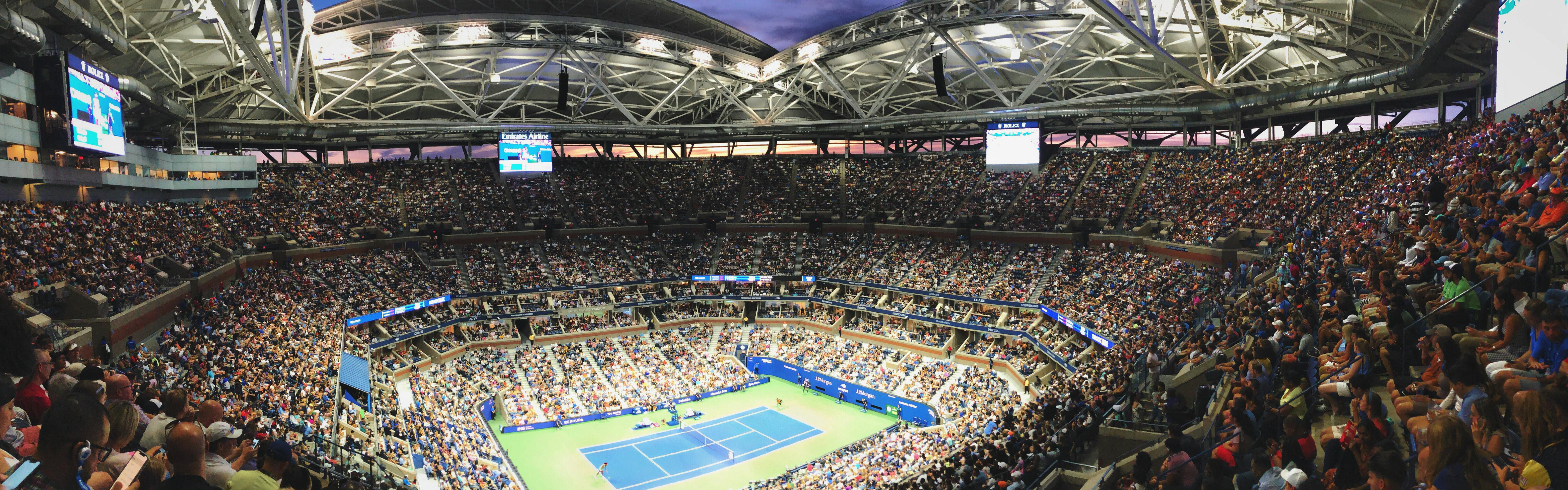 Two people playing on the Arthur Ashe stadium in the U.S. Open. The crowds are packed.