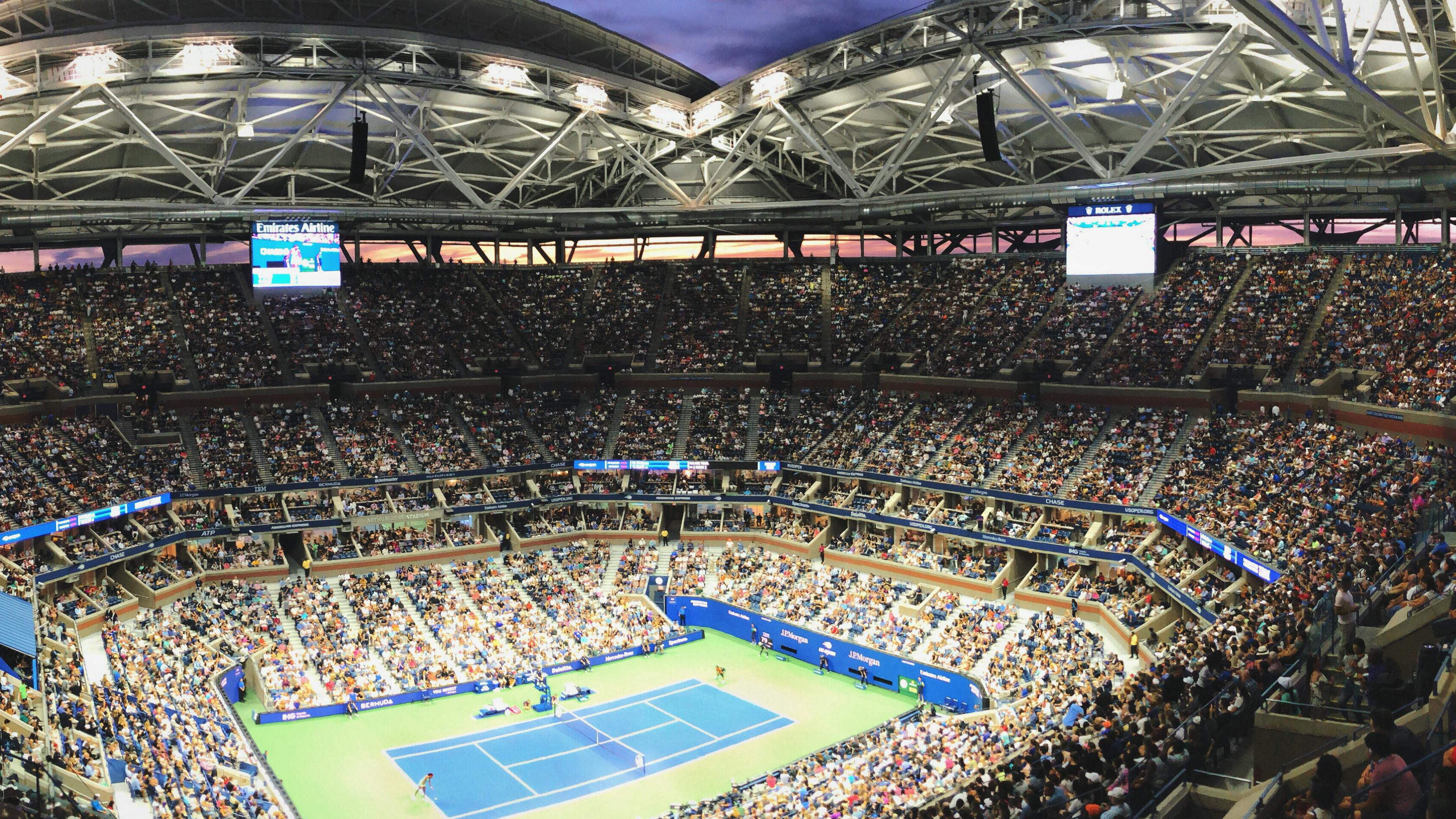 Two people playing on the Arthur Ashe stadium in the U.S. Open. The crowds are packed.