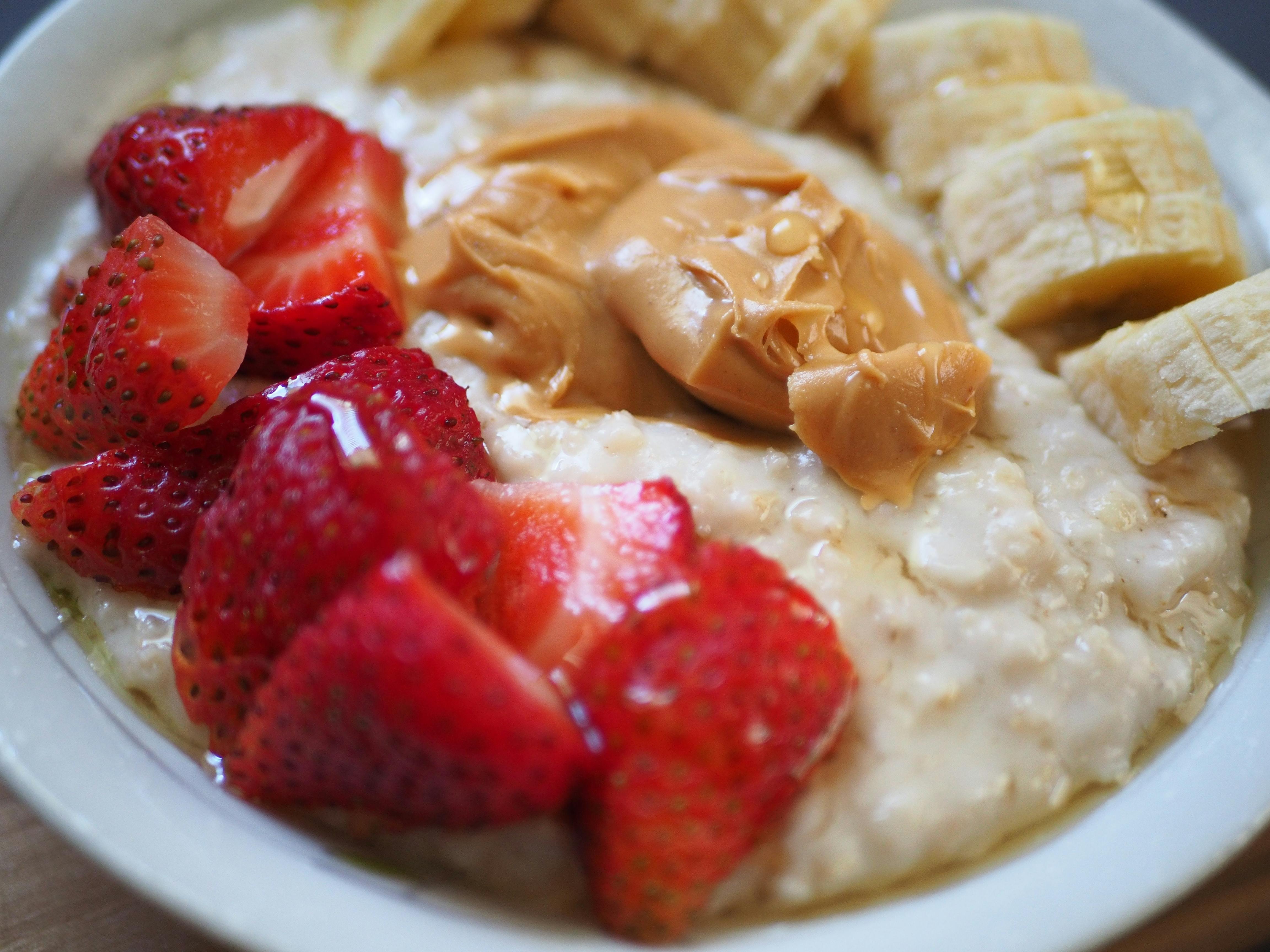 A closeup on oatmeal topped with sliced bananas, a dollop of peanut butter, and juicy red strawberries
