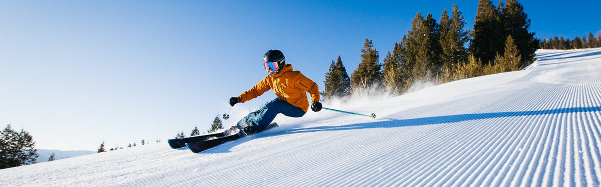 A person in an orange jacket leans into a carving ski turn