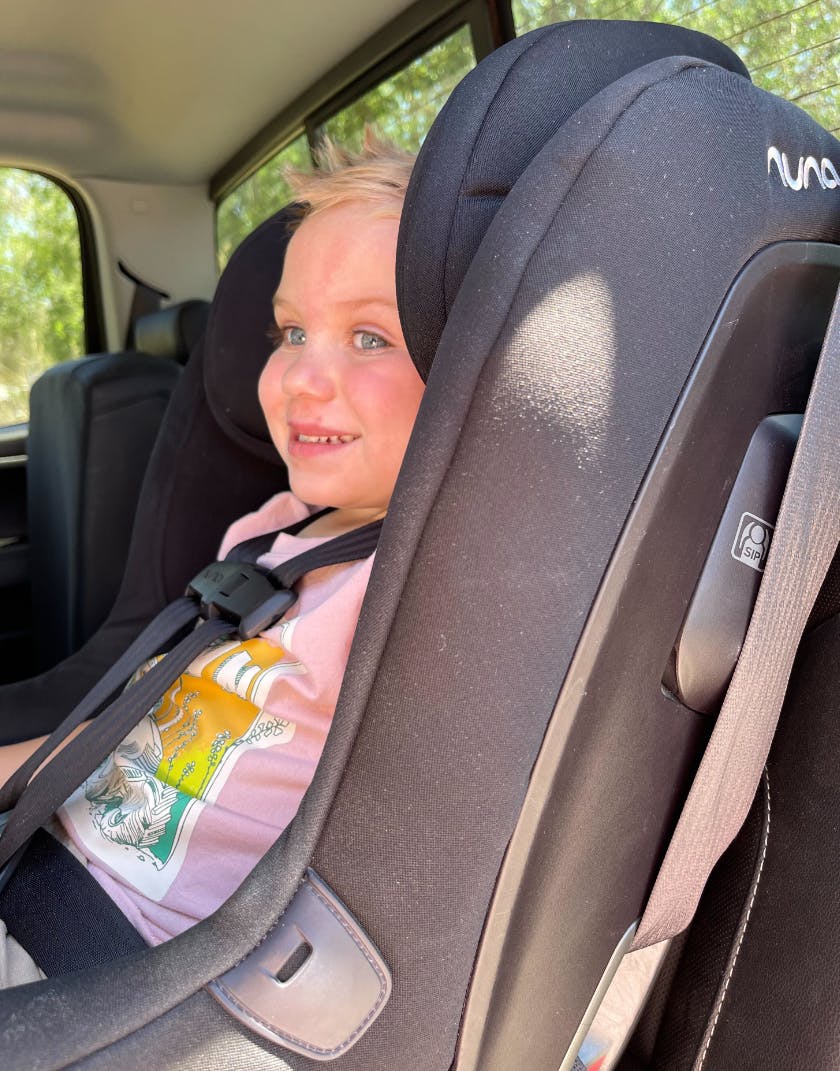 A happy baby smiles in a car seat.