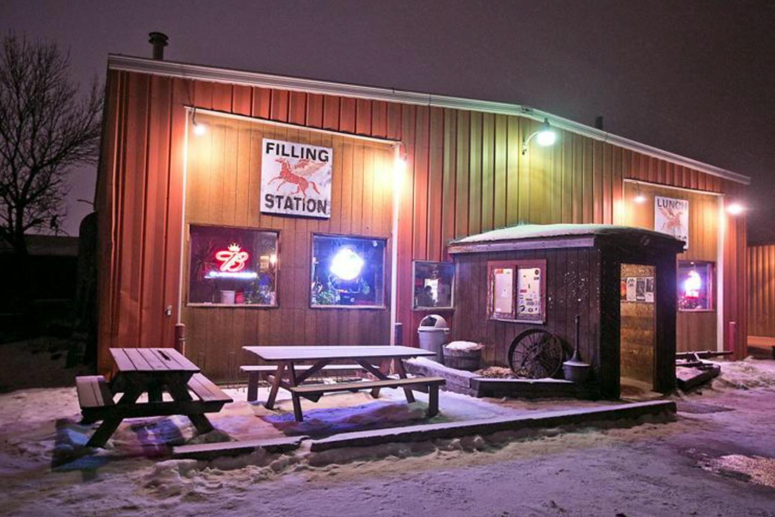 The outside of a bar in the snow. The sign says "Filling Station" and it is night time. 