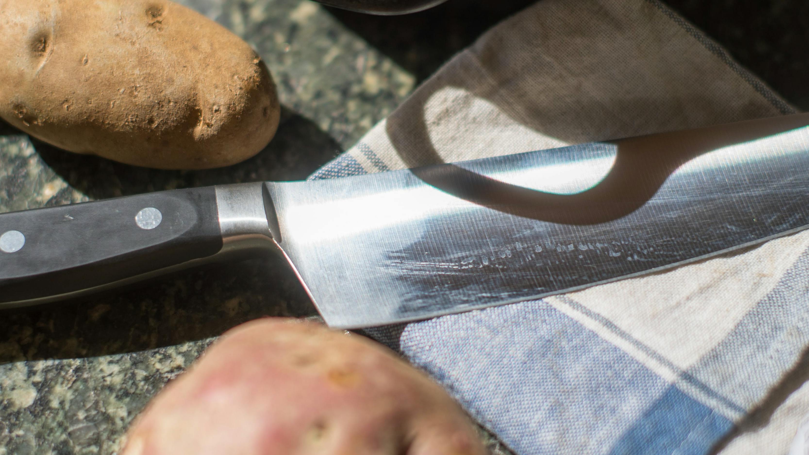 The Mercer Culinary Renaissance Forged Chef's Knife, 8 Inch lying next to some potatoes. 