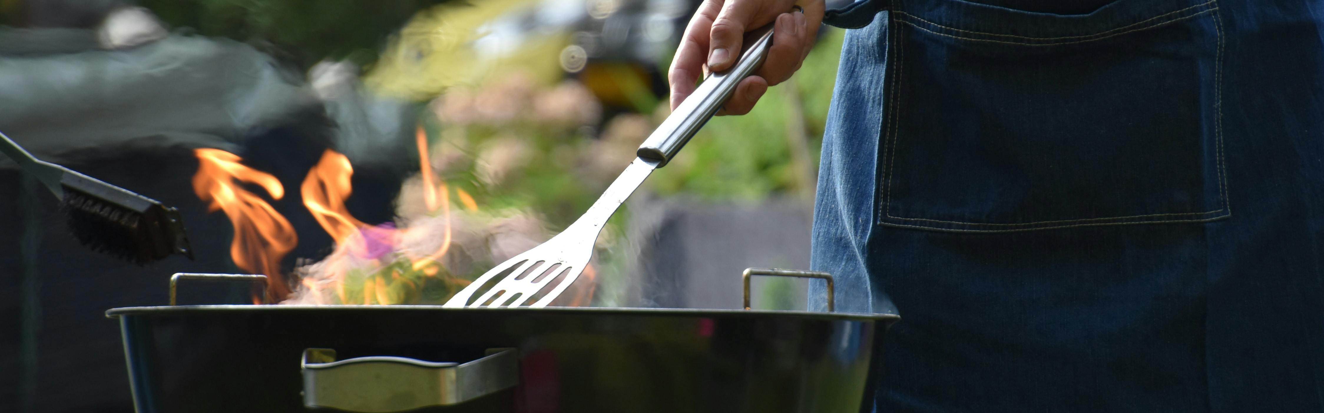 A man uses a spatula to flip a burger on a grill.