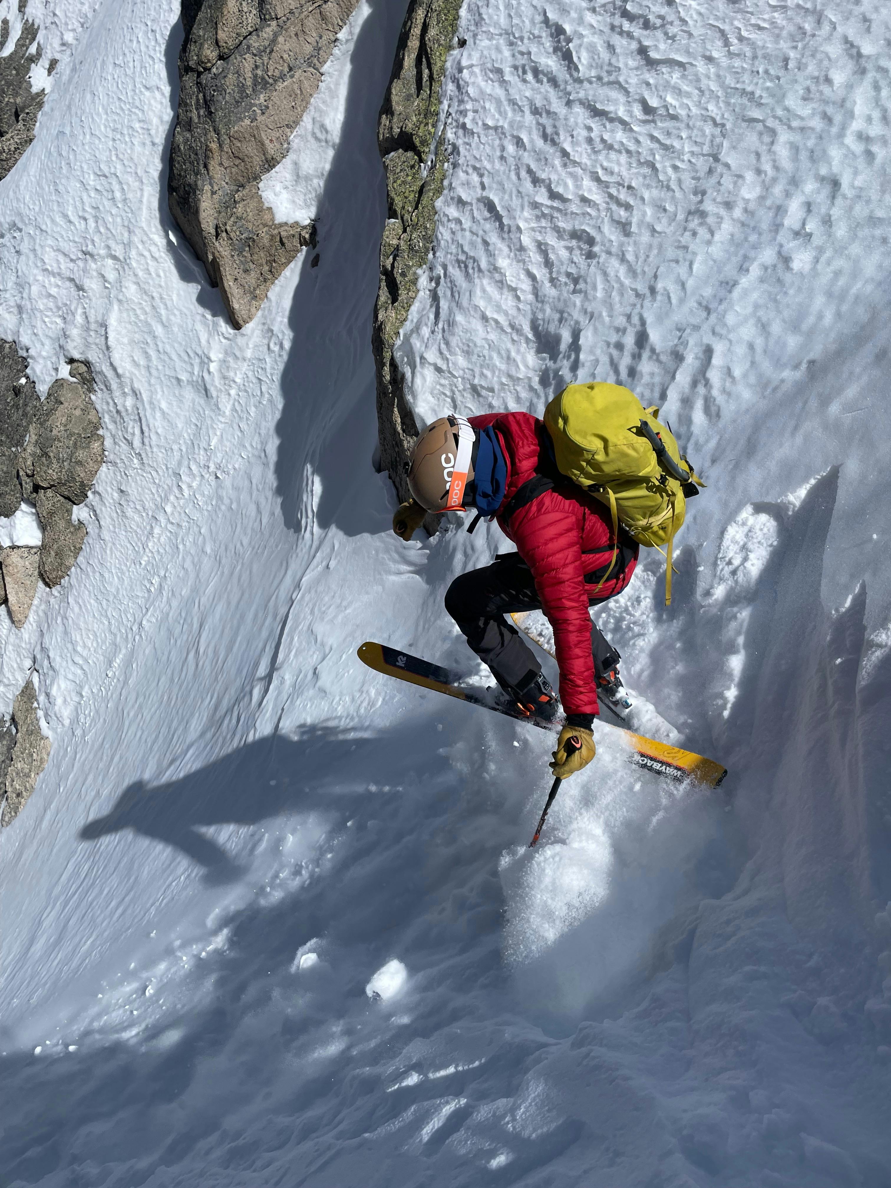 A skier heads down a narrow chute turning on top of a chunk of snow.
