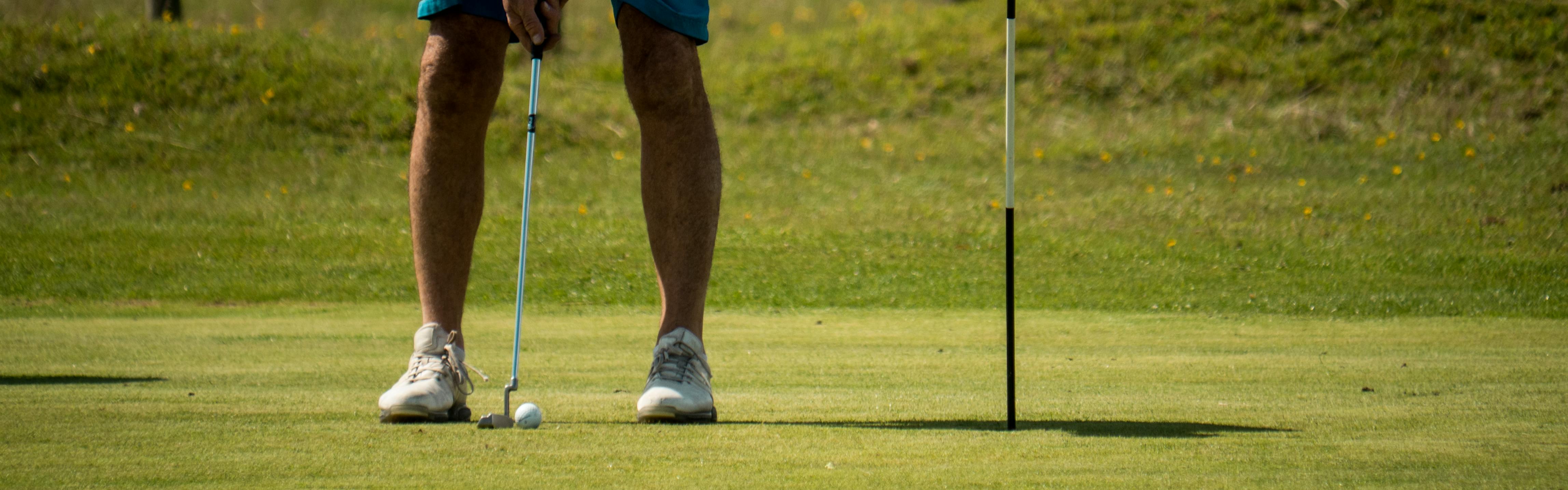 A man hits a golf ball with his putter into the hole. 