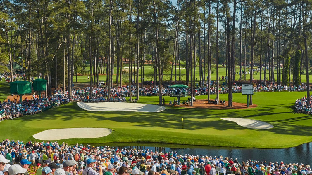 A crowd of people stands around the course at Augusta National for the Masters. 