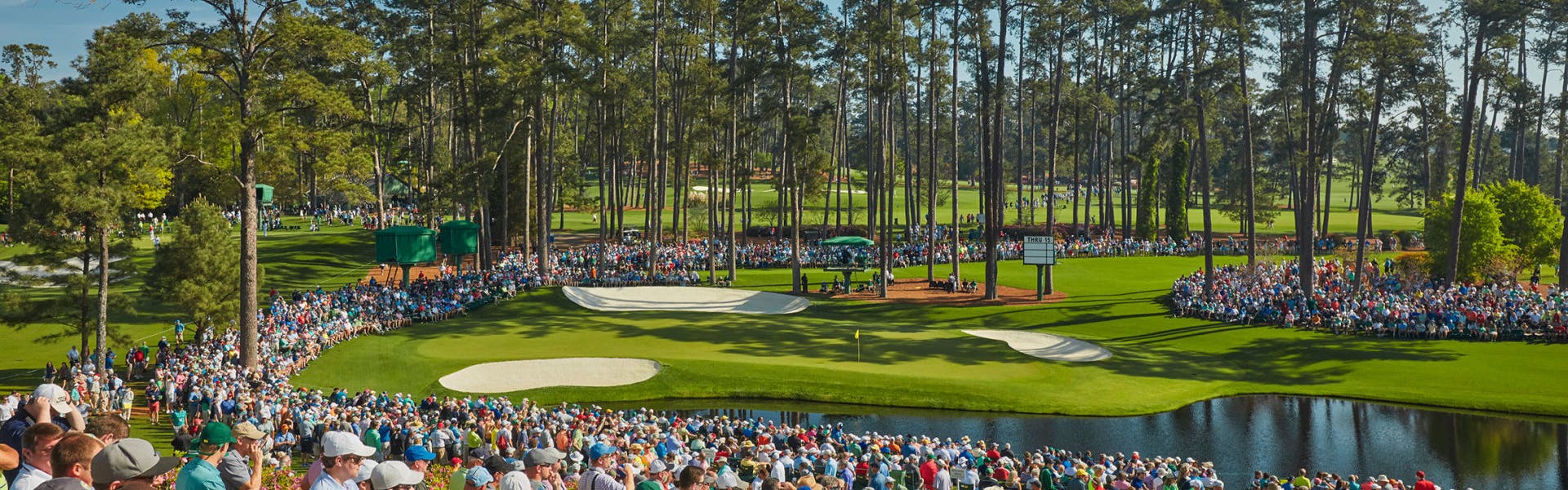 A crowd of people stands around the course at Augusta National for the Masters. 