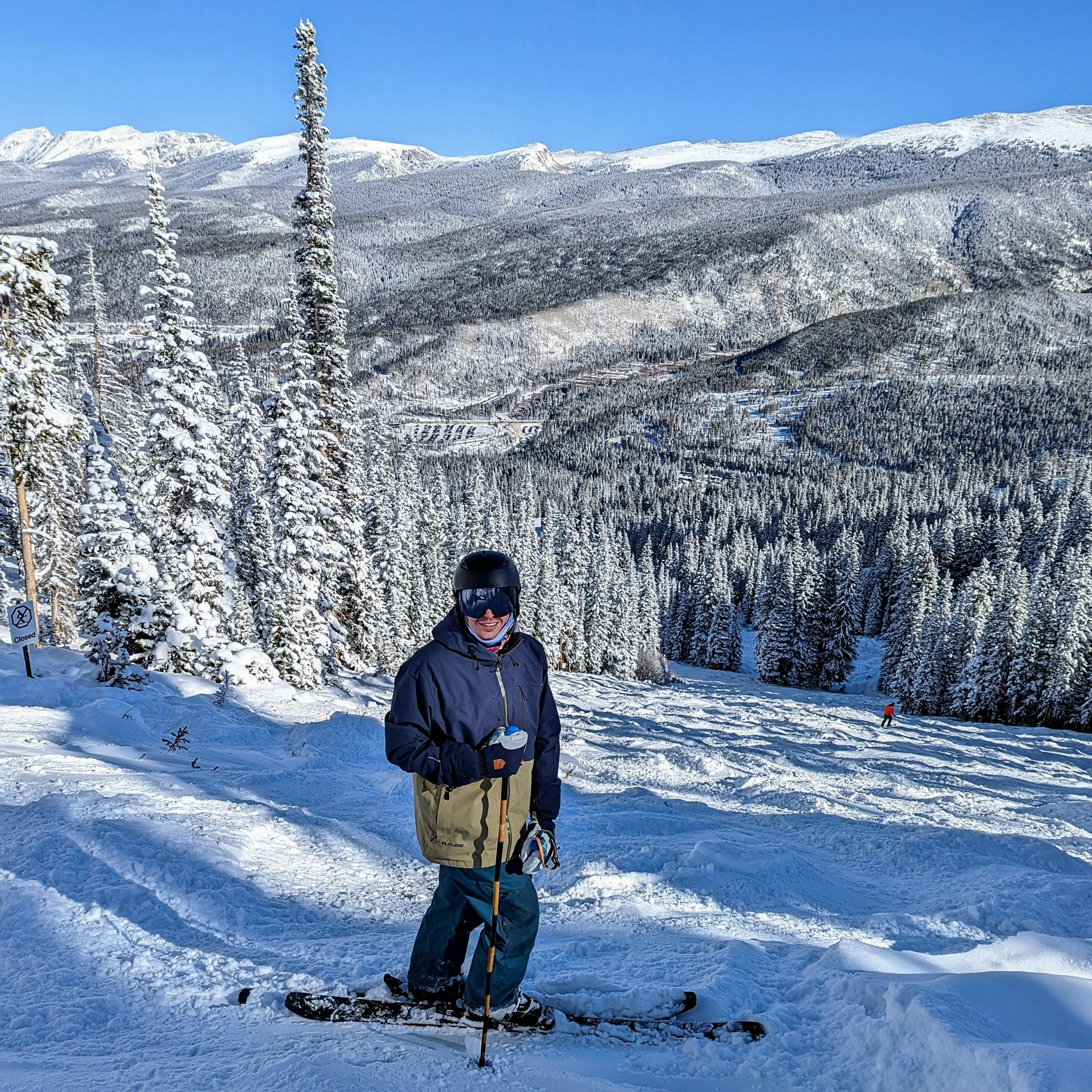 A skier standing at the top of a ski run with snowy trees in the background. 