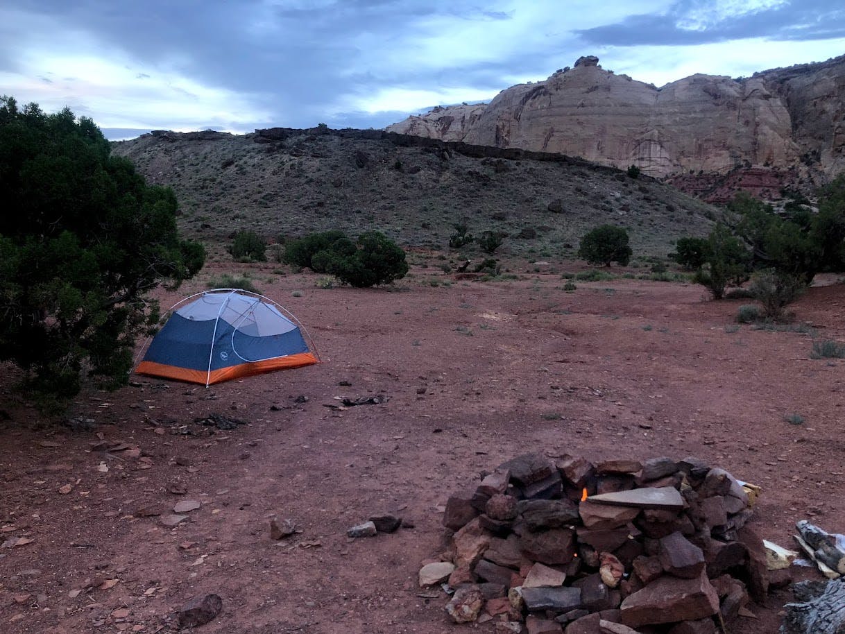 A flat campsite with a tent pitched in one corner and a large campfire in the other. It seems to be located in a desert ecosystem.