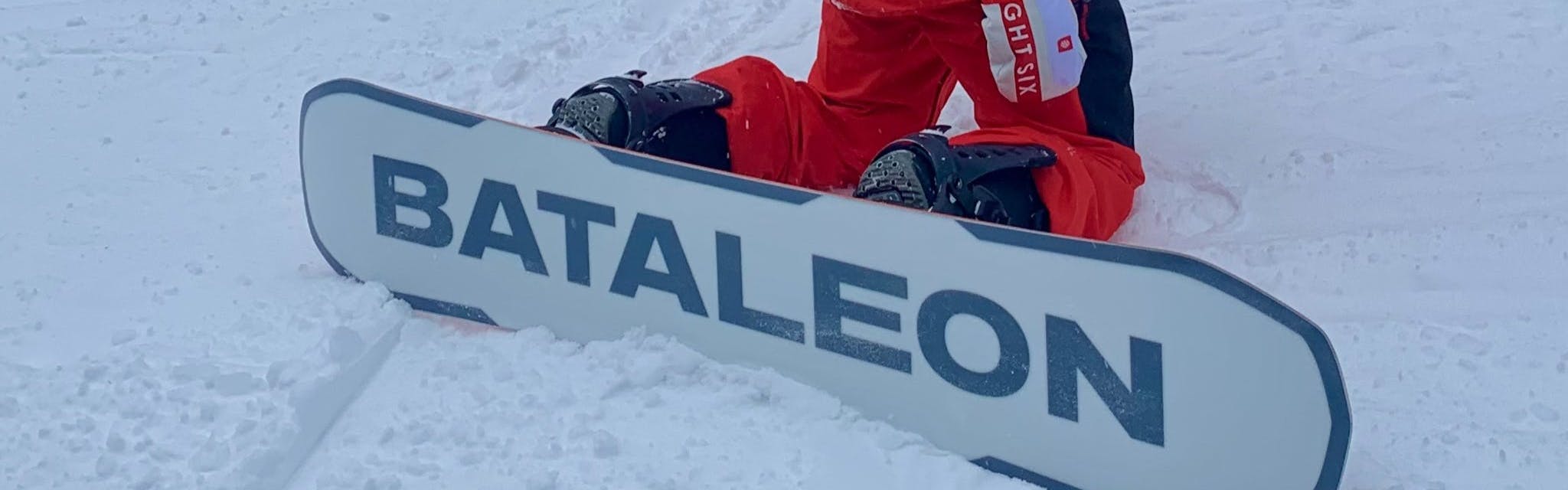 A snowboarder kneeling with the base of the Bataleon Goliath Snowboard visible. 