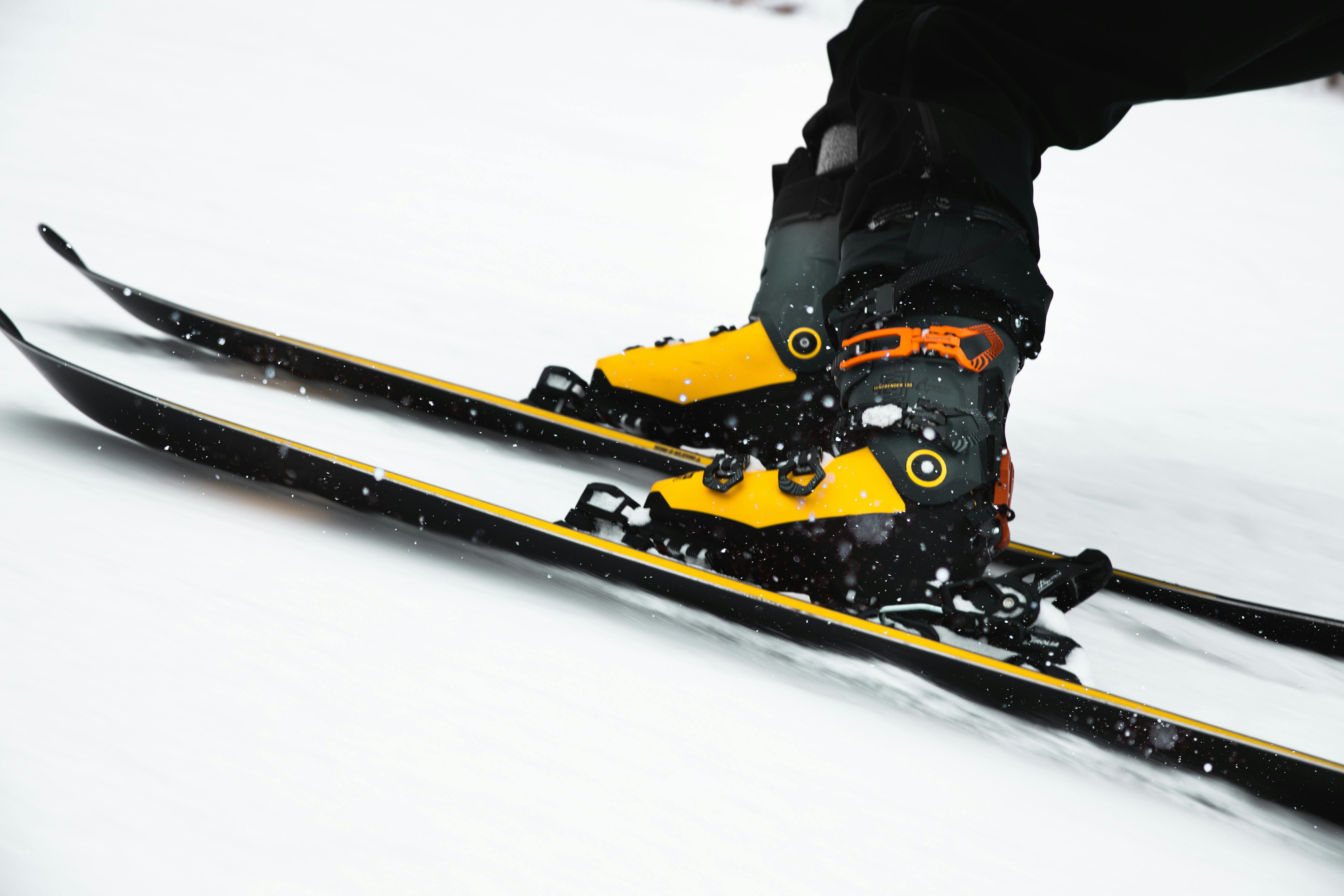 Someone skis at an angle, wearing yellow and black ski boots. 