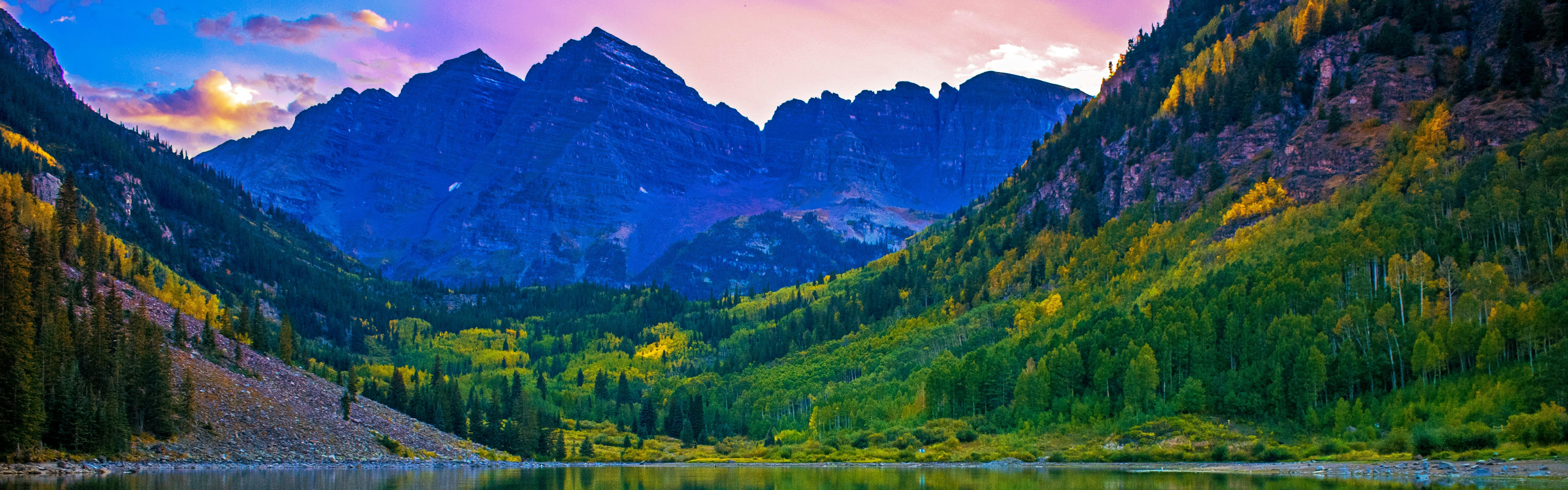 A lake sits at the base of massive mountains. The sky is pink and blue above. 