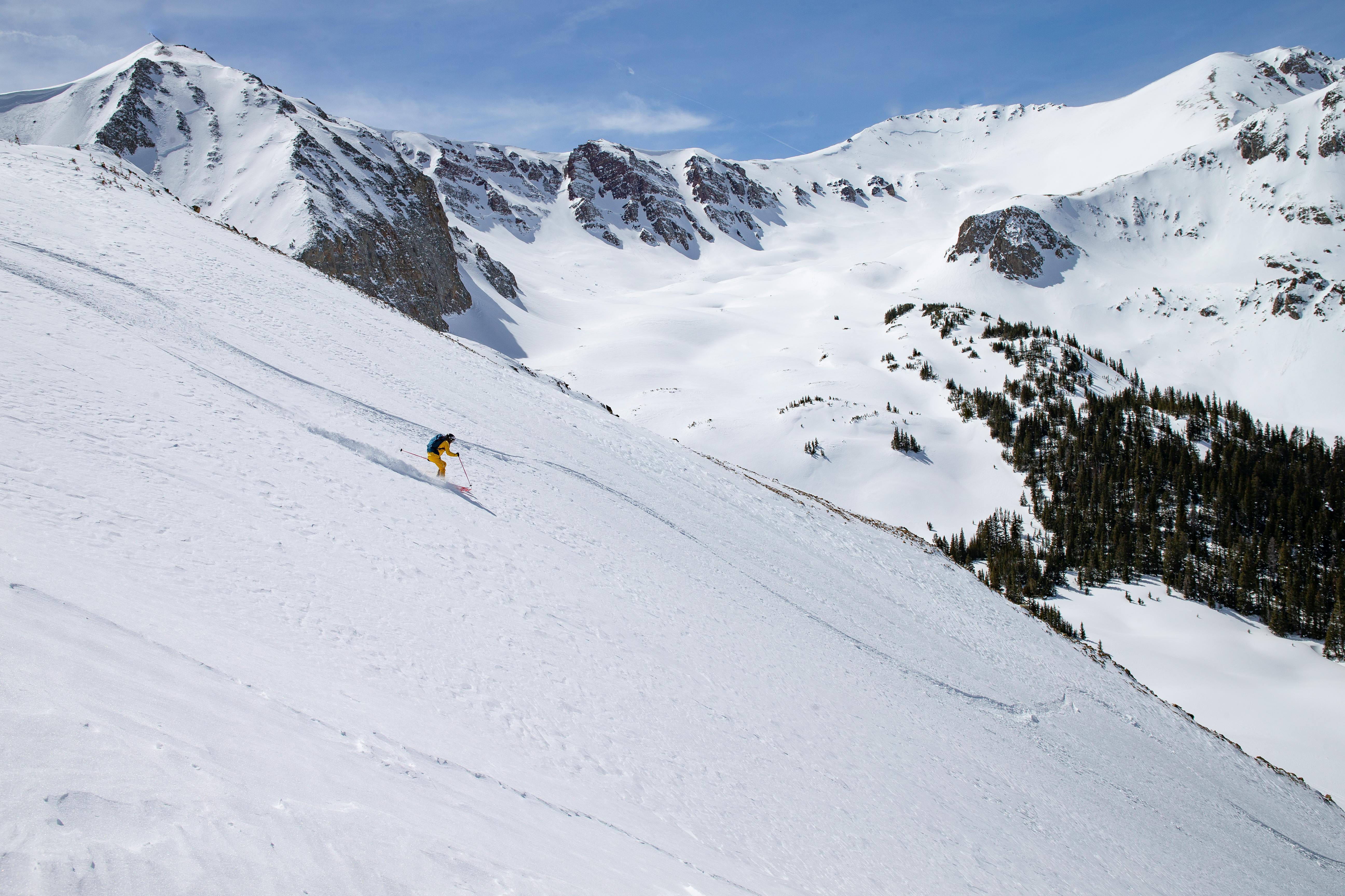A solo skier bombing down a steep backcountry slope.