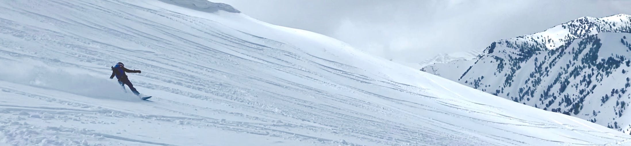 A woman on a snowboard turns down a peak. There are mountains in the background.
