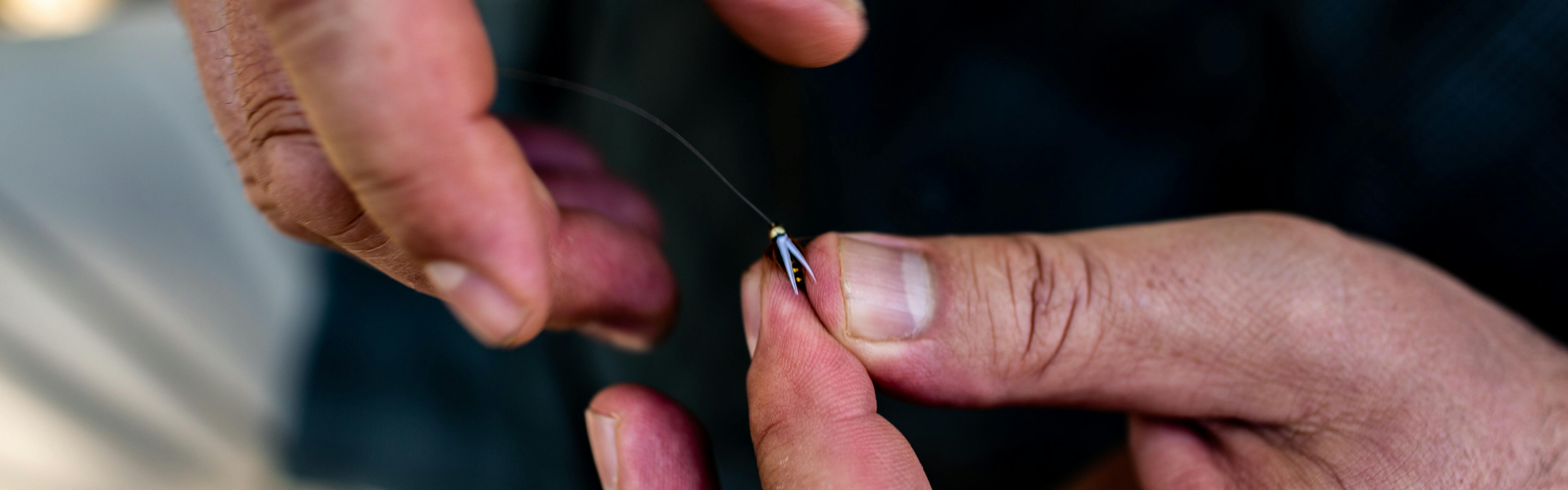 A man pinches a fly fishing fly between his fingers. 