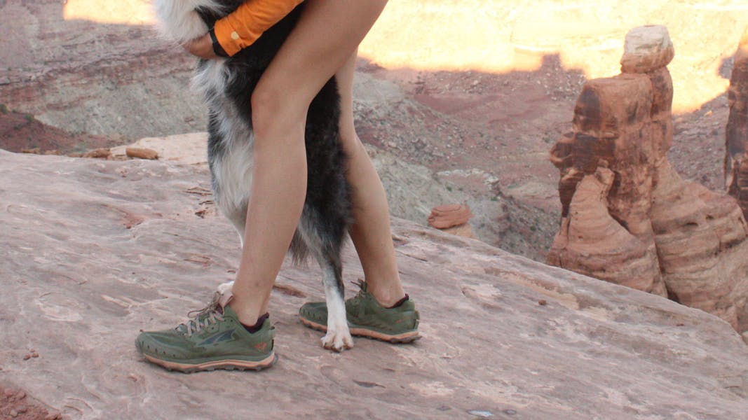 A pair of Altra Lone Peak 6's with some dog feet. There are red rocks in the background. 