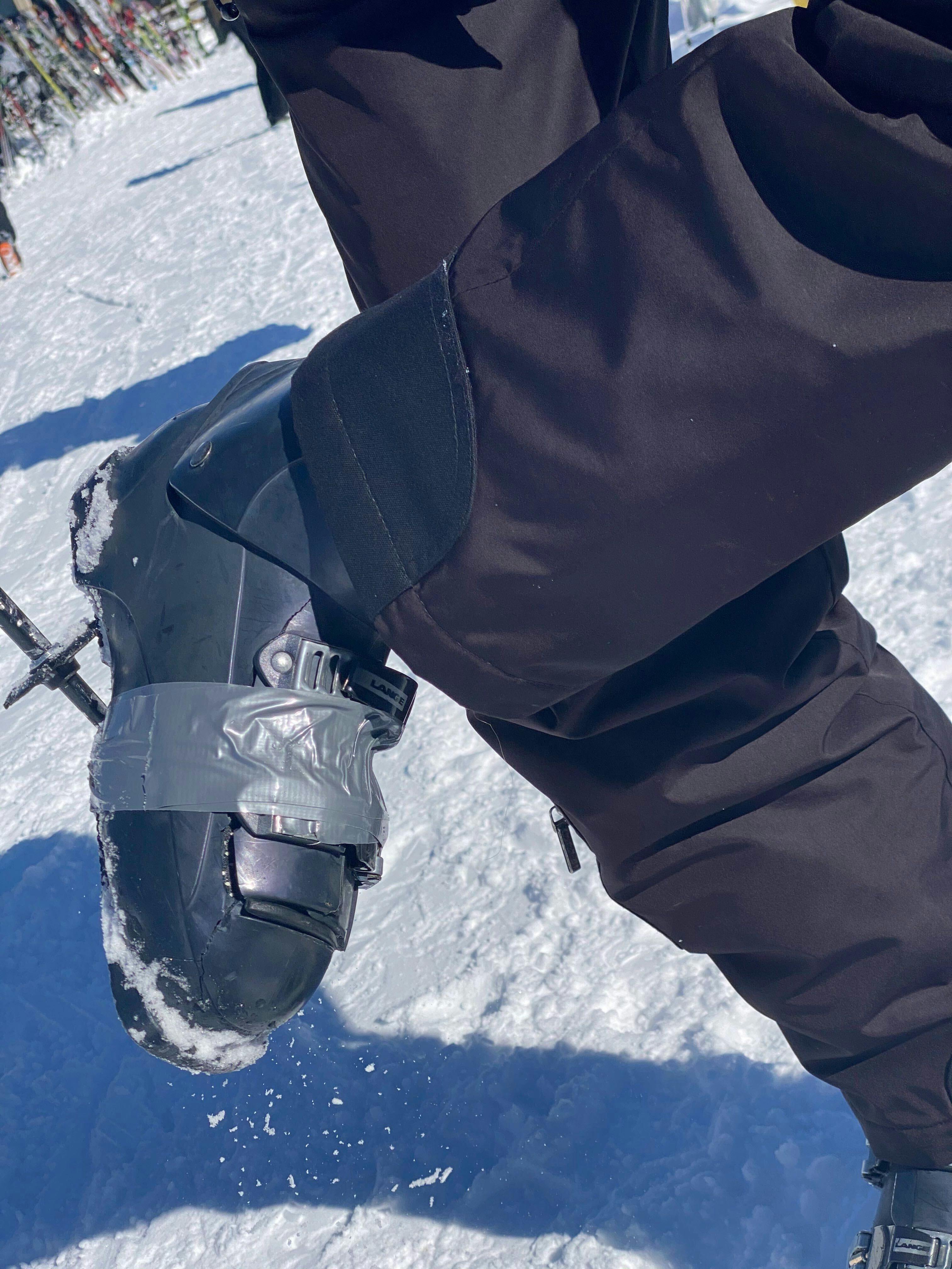 A person shows off their ski boots, which have been wrapped with duct tape