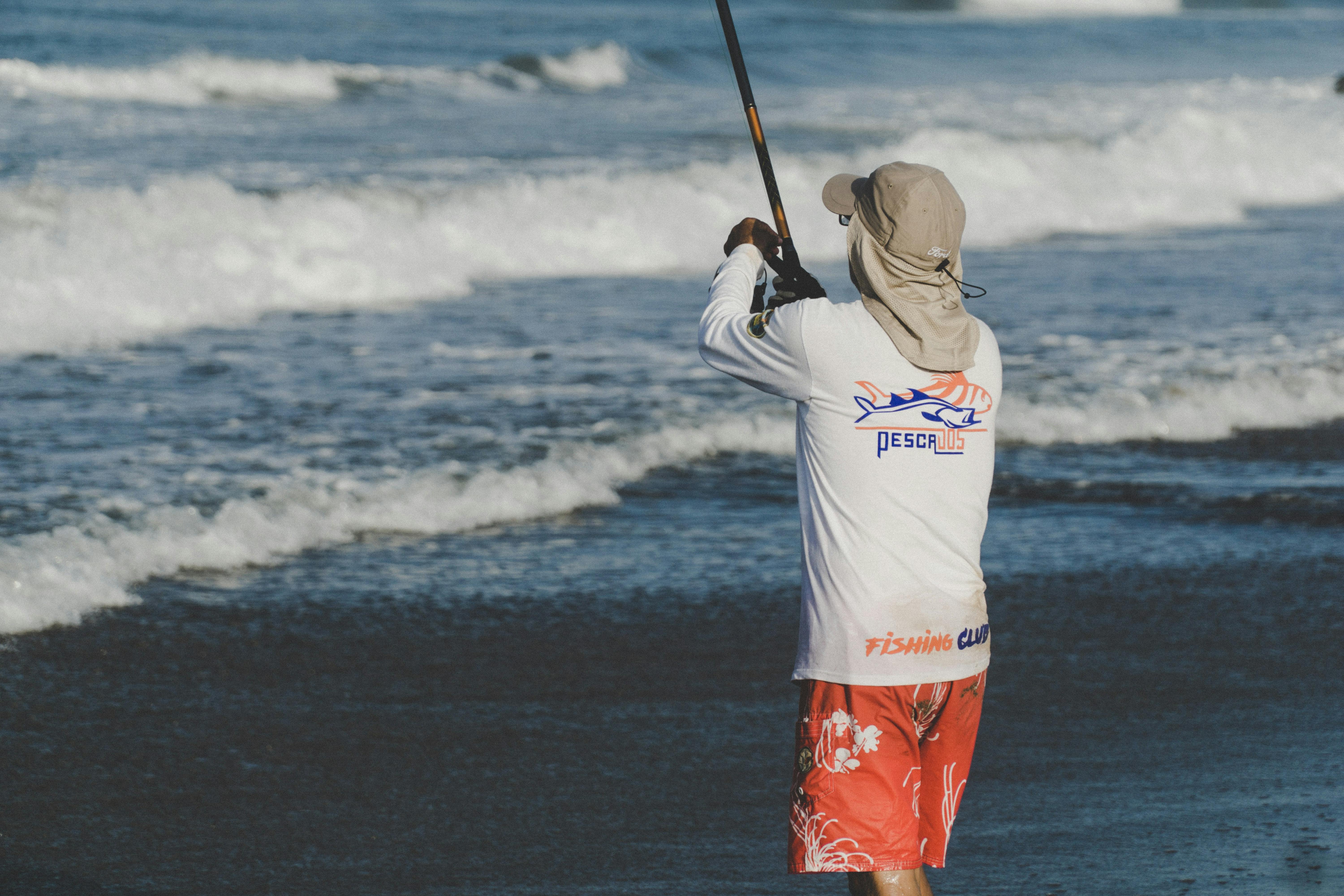 A man standing on a beach with a fishing rod. 